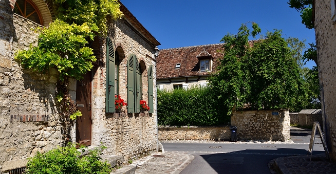 Rue fleurie d'un village avec maison en pierre et volets verts